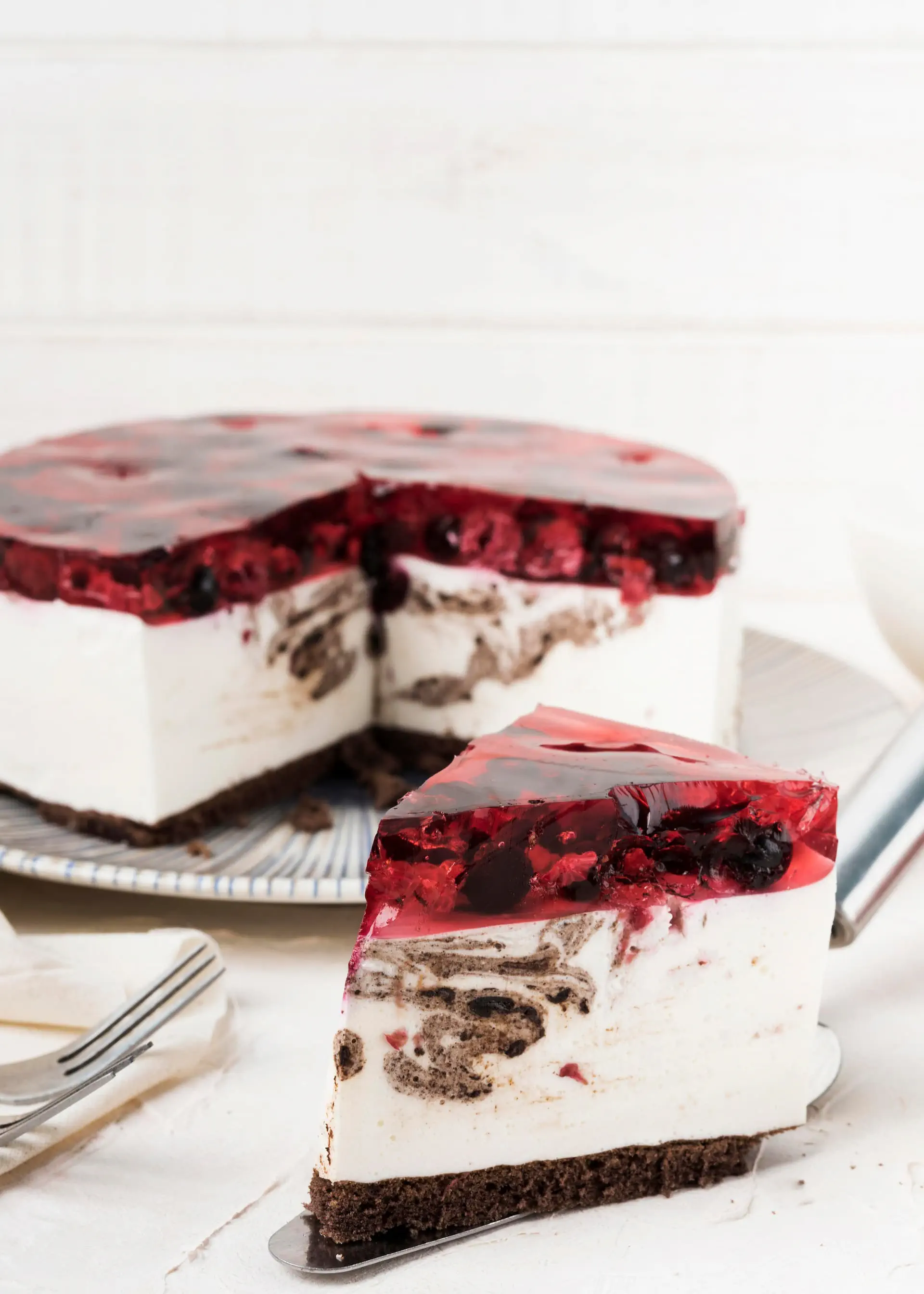 Puszysty sernik na ciemnym spodzie z galaretką i owocami leśnymi