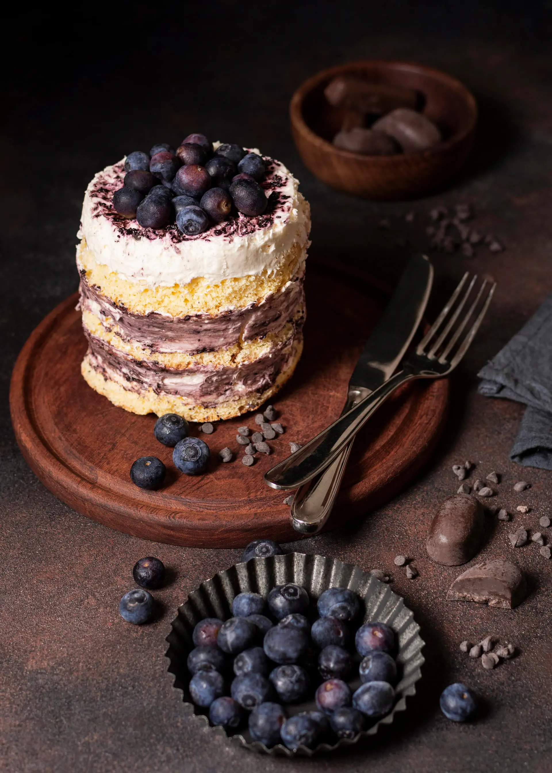 Mały tort rzemieślniczy z kremem jagodowym, udekorowany świeżymi borówkami na drewnianej desce