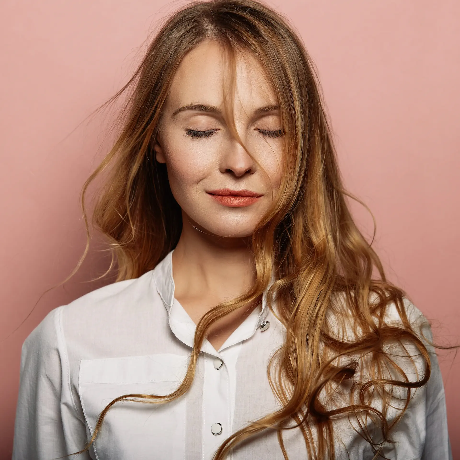 Portret dziewczyny o blond włosach z delikatnymi falami na jasnoróżowym tle