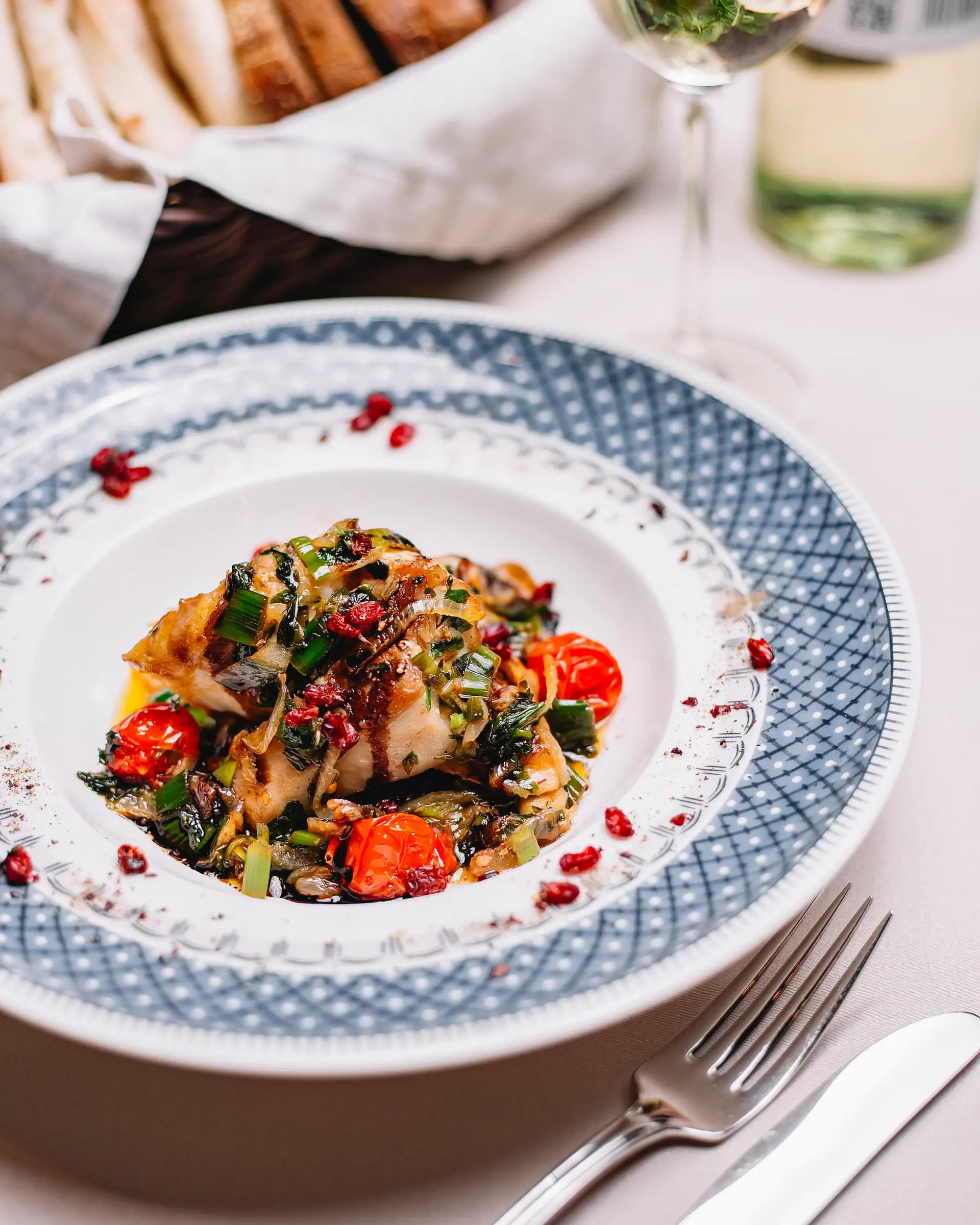 Portfolio gastronomia: Elegancko podana pieczona ryba z duszonymi warzywami, pomidorkami koktajlowymi i świeżymi ziołami