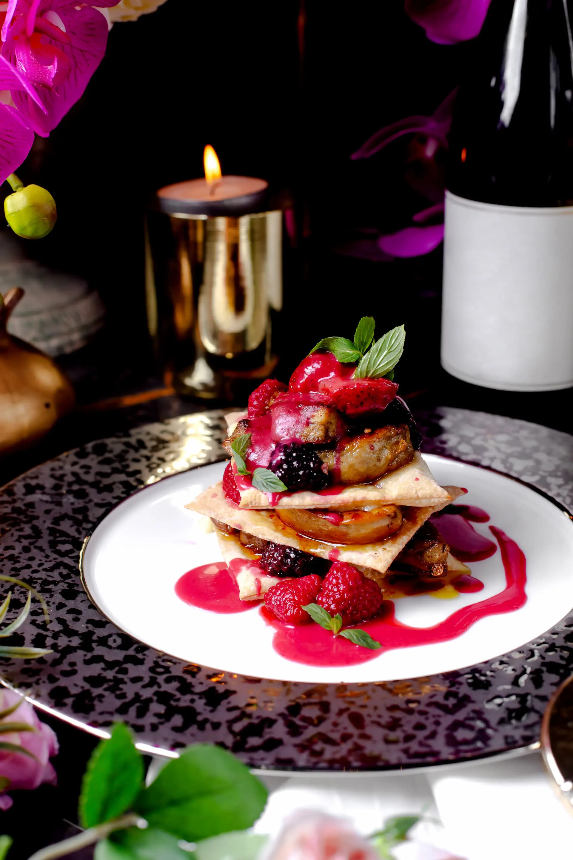 Portfolio gastronomia: Wykwintny deser warstwowy z owocami leśnymi, musem i świeżą miętą, podany na dekoracyjnym talerzu przy blasku świecy