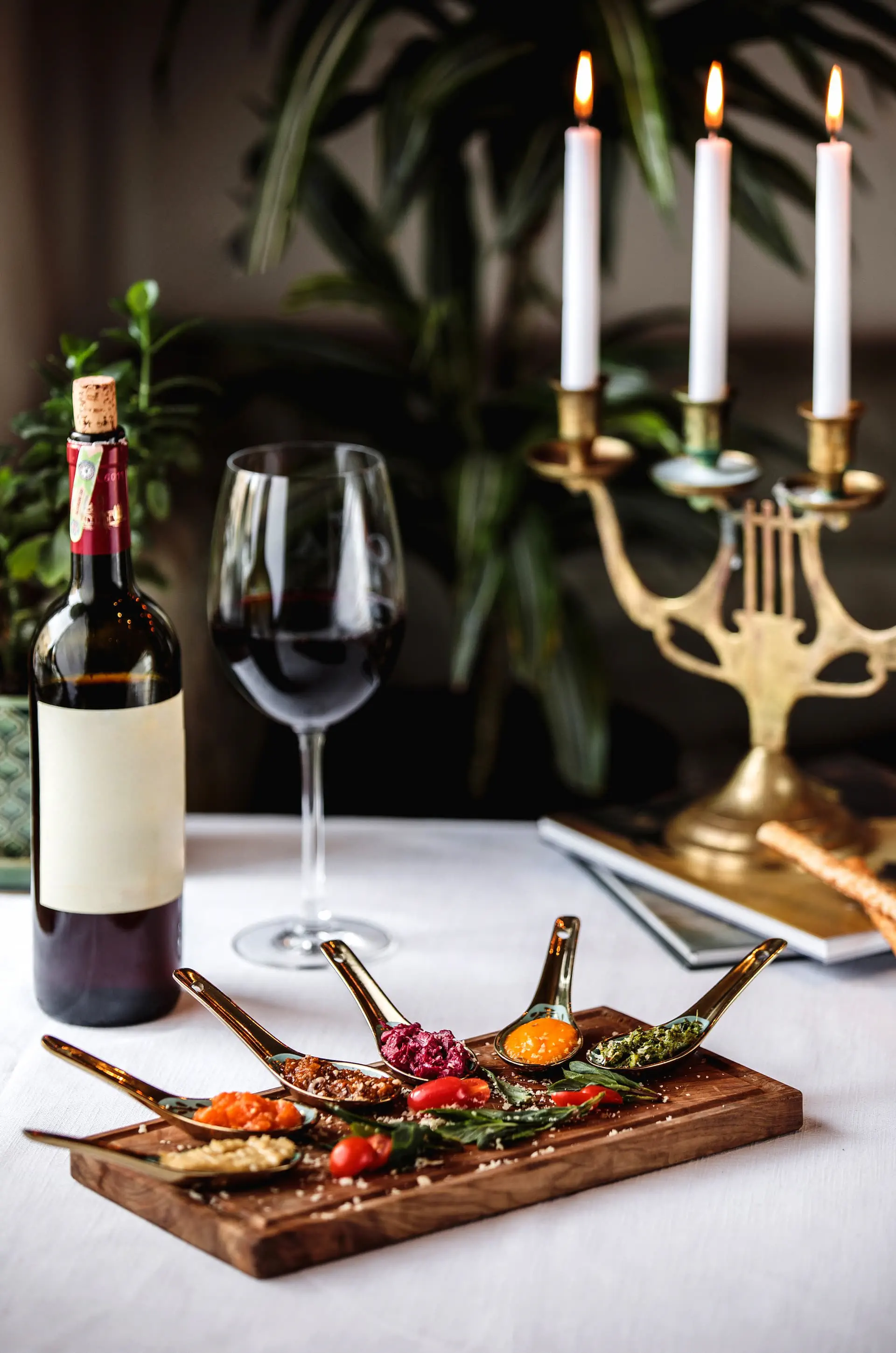 Kategoria menu: Wina i Przystawki - butelka czerwonego wina, kieliszek oraz zestaw kolorowych tapas serwowanych przy blasku świec